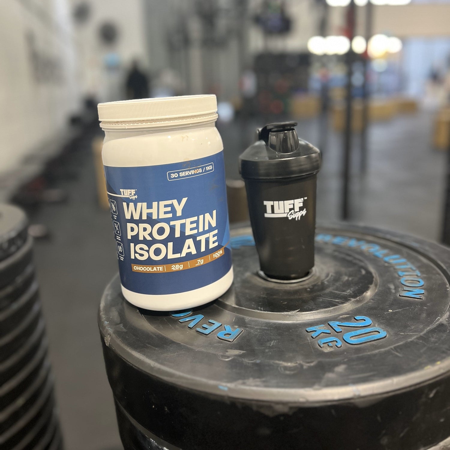 Whey protein isolate container and shaker on a weight plate in a gym setting