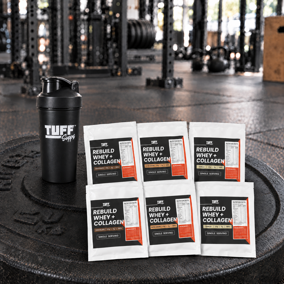Rebuild Whey + Collagen sample sachets and a Tuff Supps shaker on a weight plate in a gym